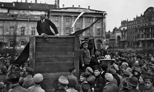 Lenin spricht von einer improvisierten Bühne zu einer großen Menschenmenge. Die Szene wirkt wie eine "revolution von oben", die das Volk mobilisiert.