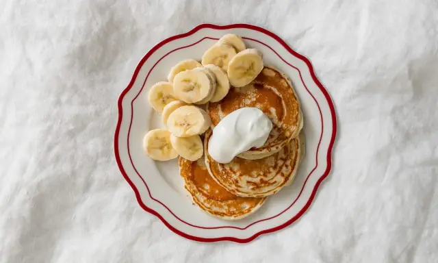 Placuszki bananowe dla niemowlaka na talerzyku z kremem i plasterkami banana.