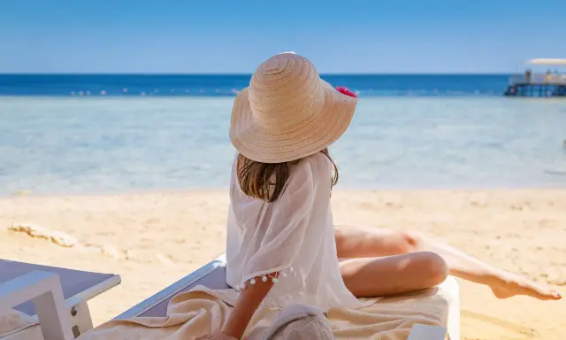 Dziewczynka w kapeluszu na plaży, marząca o tym, gdzie warto polecieć. Piękne morze i słońce zachęcają do odpoczynku.