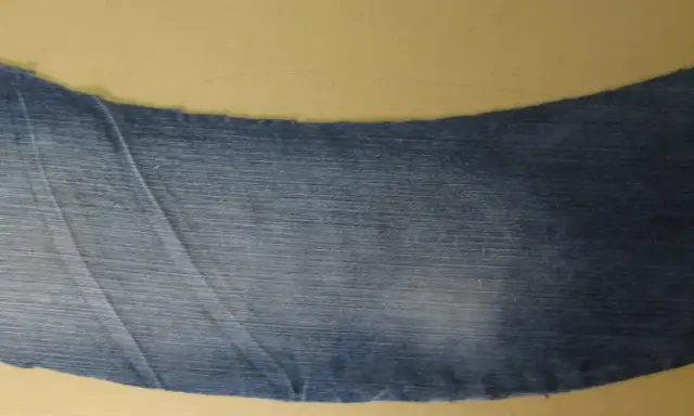 Ett utskuret jeansstycke med en vågig kant, redo att sys till en volang. Röd tråd syns längs ena sidan.