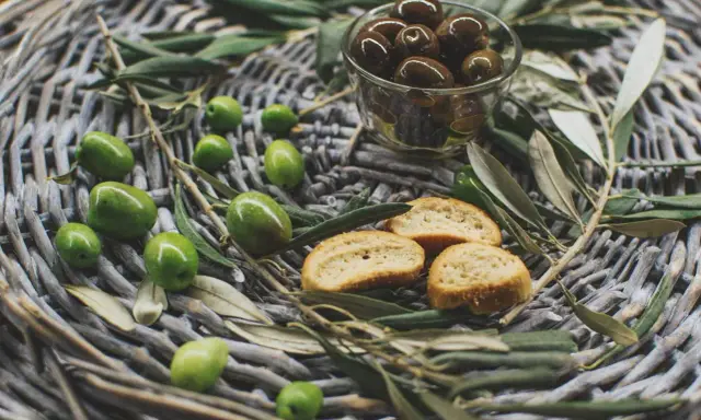 Olives vertes et noires, crostinis et feuilles d'olivier sur un panier tressé, évoquant une spécialité culinaire du Luberon.