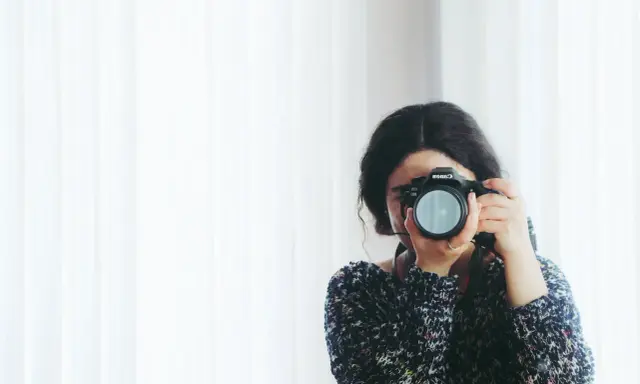 Kobieta z aparatem Canon, skupiona na kadrze. Rozwija swój biznes fotograficzny, łapiąc chwile.