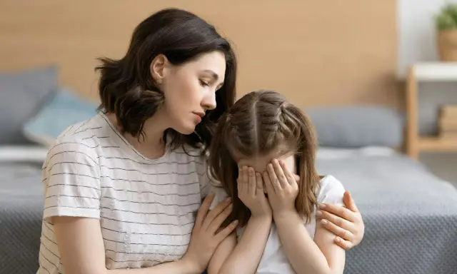 Eine Mutter tröstet ihr weinendes Kind, das sich die Augen zuhält. Möglicherweise kämpft das Kind mit Zwangsgedanken bei Kindern.