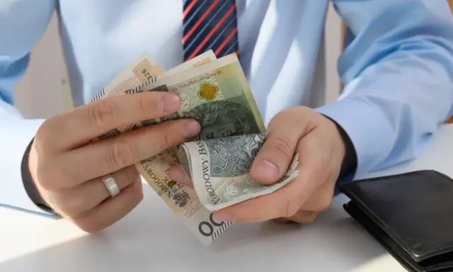 Dłonie liczą polskie banknoty. Zastanawiasz się, ile pracodawca płaci za pracownika przy najniższej krajowej?