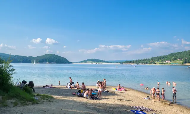 Polańczyk atrakcje: plażowicze odpoczywają nad Soliną, w tle żaglówka i zielone wzgórza.