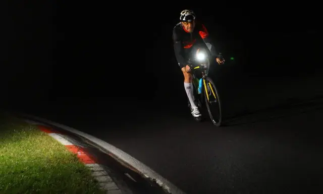 Kolarz w kasku z czaszką jedzie nocą, oświetlając drogę mocnym światłem. Czy rower musi mieć włączone światła w dzień? To pytanie nabiera sensu, gdy widzimy taką jazdę.