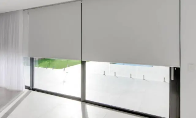 Elegantes persianas enrollables grises ofrecen soluciones para ventanas con mucho sol, bloqueando el deslumbramiento y el calor.