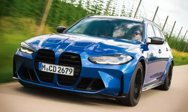 Blauer BMW M3 Competition Kombi rast auf einer Landstraße, die Sonne spiegelt sich im Lack.