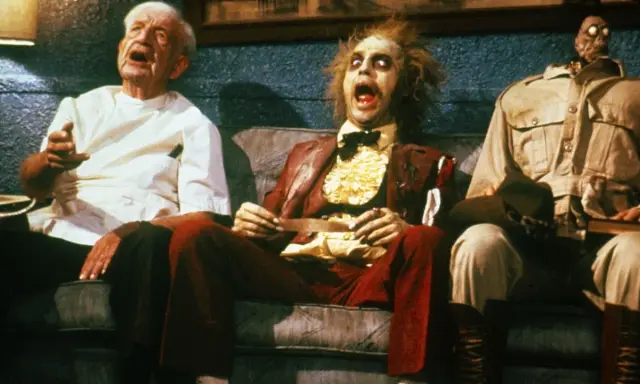 Tre personaggi bizzarri, tra cui Beetlejuice, siedono su un divano in una scena di horror comedy.