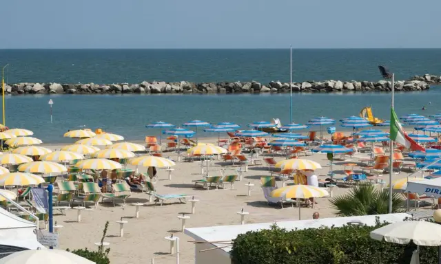 Spiaggia affollata con ombrelloni gialli e bianchi, lettini e il mare azzurro. Un'immagine di igea marittima, perfetta per una vacanza.