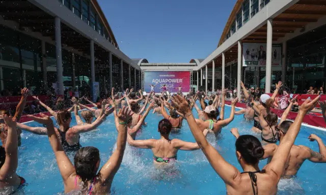 Folla entusiasta partecipa a una lezione di acquagym all'aperto, con le braccia alzate, durante la fiera dello sport Rimini.