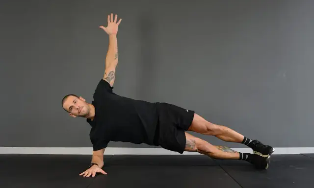 Uomo in posizione di side plank, con un braccio sollevato e l'altro appoggiato a terra.