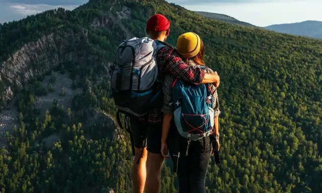 Para spacerowiczów w górach we wrześniu. Wygodne ubranie, plecaki i piękny widok na las.
