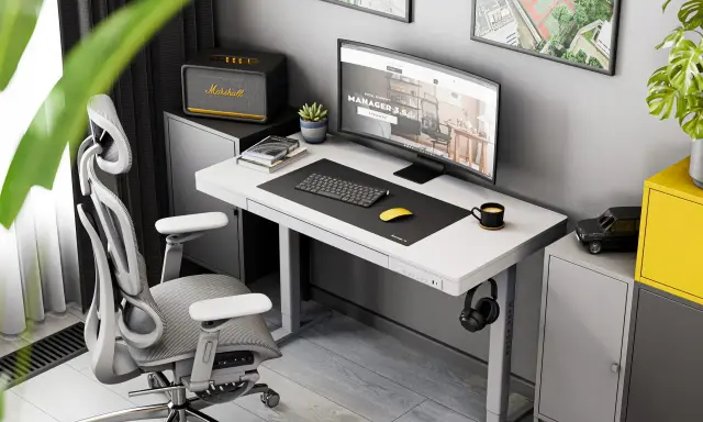 Ergonomiczne biurko do pracy przy komputerze z monitorem, klawiaturą i myszką. Obok stoi wygodny fotel biurowy i szafka z głośnikiem Marshall.