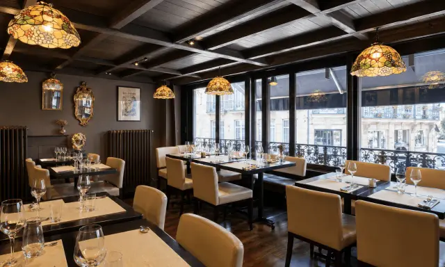 Salle à manger élégante avec des tables dressées, des luminaires Tiffany et une affiche "Les Artistes Limoges Menu" au mur.