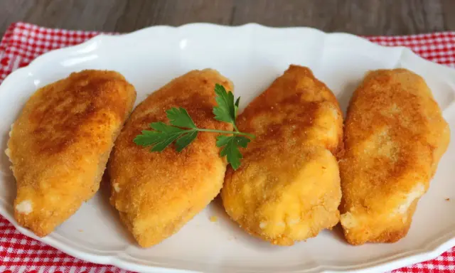 Cuatro pechugas villaroy doradas y crujientes, servidas en un plato blanco con una ramita de perejil.
