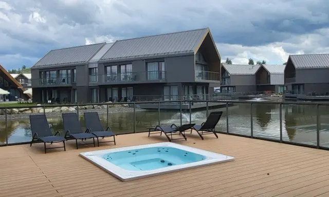 Relaks przy jacuzzi i basenie z widokiem na nowoczesne domki nad wodą. Idealne miejsce na wypoczynek w stylu termy Karkonosze.