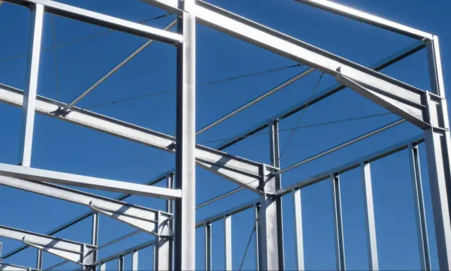 Structure métallique d'un bâtiment en construction, avec des poutres et des poteaux d'acier sous un ciel bleu clair.