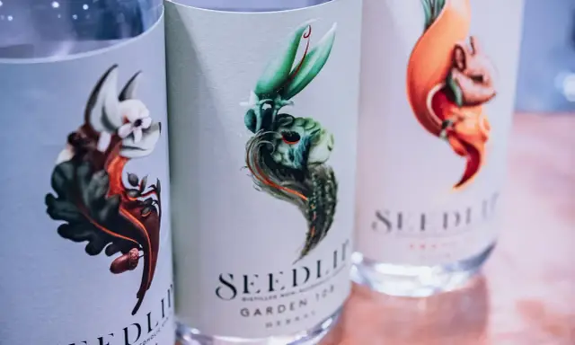 Drei Flaschen Seedlip alkoholfreien Gin mit kunstvollen Etiketten, die fantasievolle Tiere und Pflanzen zeigen.