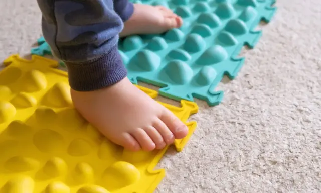 Dziecko stąpa po kolorowych matach sensorycznych. Czy zaburzenia integracji sensorycznej to autyzm? To pytanie nurtuje wielu rodziców.