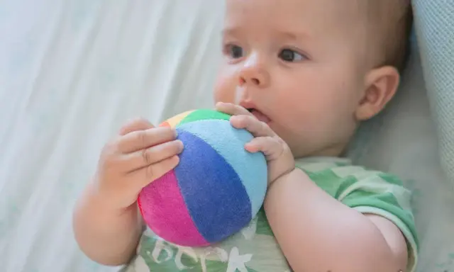 Bebé explorando el mundo con su sentido tacto, agarrando una pelota de colores.