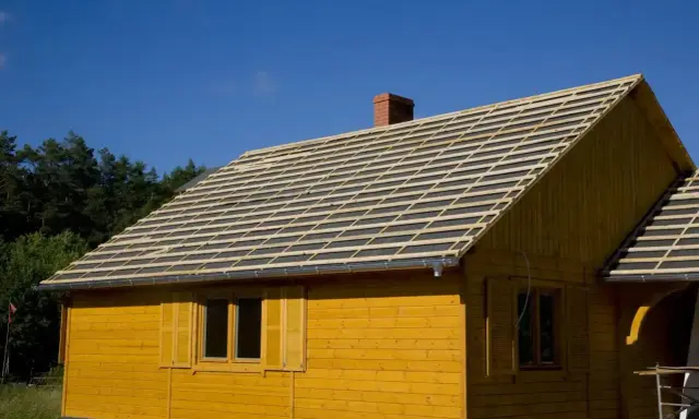 Żółty domek z widocznym pełnym deskowaniem dachu, przygotowanym pod pokrycie.