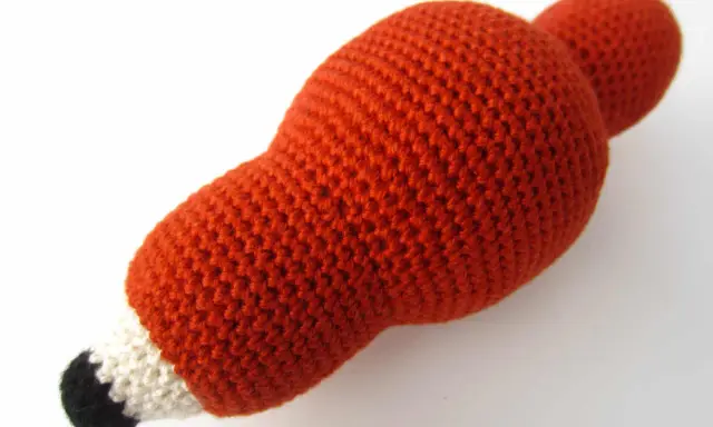 Un adorable zorro amigurumi de lana naranja, con detalles blancos y negros en el hocico, listo para jugar.