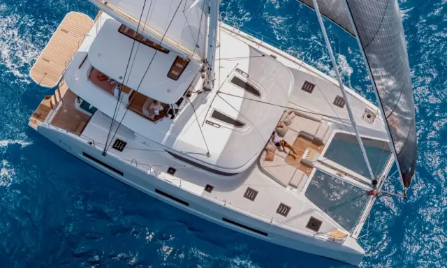 Un catamaran sans voile glisse sur l'eau bleue. Une personne se repose sur le pont, profitant du soleil.