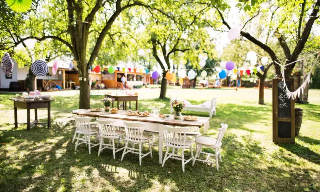 Une table dressée pour un repas en plein air, avec des guirlandes et des ballons, évoque une ambiance de deco jardin boheme chic.