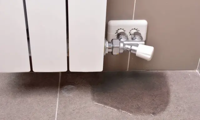 Un radiador que gotea deja un charco de agua en el suelo de baldosas, señal de un problema de fontanería.