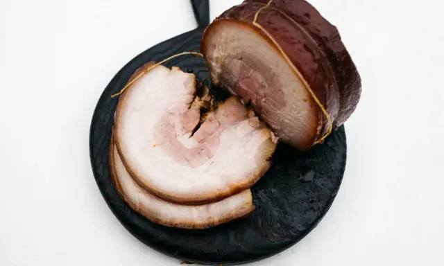 Pokrojony boczek chashu, z widocznymi warstwami mięsa i tłuszczu, ułożony na ciemnej desce.