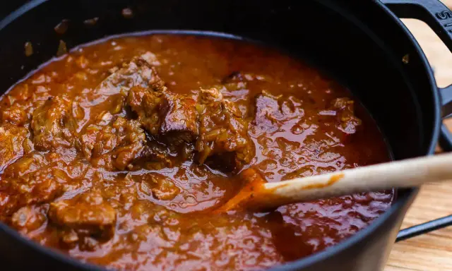 Ein dampfender Topf mit zartem Wiener Saftgulasch, das mit einer Holzschaufel umgerührt wird.