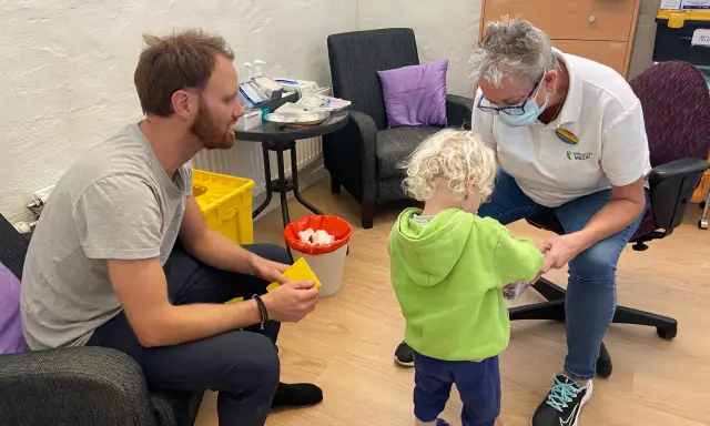 En pappa och ett barn får vaccin av en sjuksköterska. Barnet verkar lite oroligt, men sjuksköterskan är lugn och trygg. Det är en fin stund av vaccin italien.