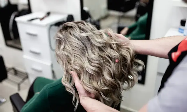 Profesjonalne usługi fryzjerskie: stylista układa falowane, blond włosy klientki w salonie.