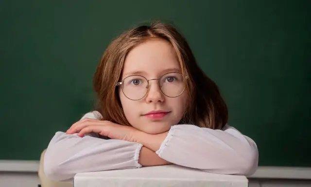 Dziewczynka w okularach opiera głowę na stosie książek. Zastanawia się, do kiedy można pobierać zasiłek rodzinny.