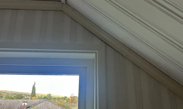 Takskena i snedtak med panelklädda väggar. Fönstret ger utsikt över hus och höstfärgad natur.