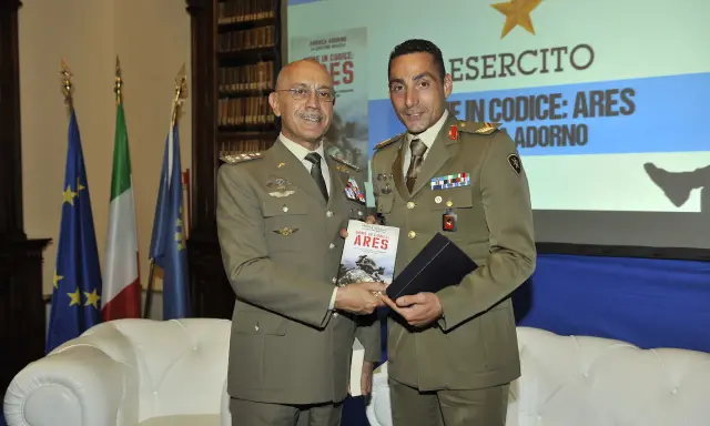Due ufficiali in uniforme presentano un libro. Uno dei due, con un sorriso, tiene in mano il volume intitolato "Nome in codice: Ares", un'opera che narra storie di coraggio, forse ispirate a un vero pesce monaco.