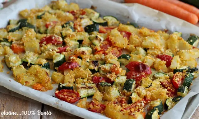 Un vassoio di verdure al forno, con patate, zucchine e pomodorini, condite con pangrattato dorato.