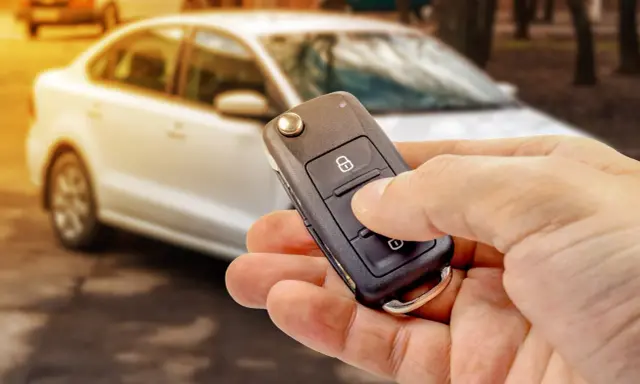 Dłoń trzyma kluczyk samochodowy z przyciskiem blokady. Czy to immobilizer? To system zabezpieczający auto przed kradzieżą.