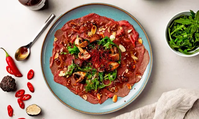 Rindercarpaccio mit Pilzen, Rucola und Mandeln. Eine köstliche Variation von Carpaccio, garniert mit Chili und Trüffel.