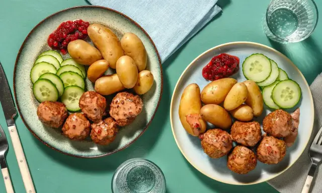 Två tallrikar med köttbullar, småpotatis, gurka och lingonsylt. En perfekt snabb middag för två.