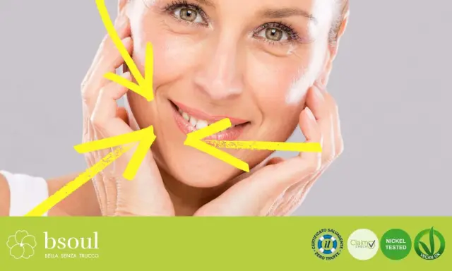 Primo piano di un volto femminile con rughe d'espressione, evidenziate da frecce gialle. Il trucco leggero esalta la bellezza naturale.