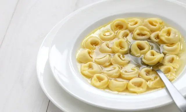 Tortellini in brodo, uno dei cibi tipici dell'Emilia Romagna, serviti in una ciotola bianca con un cucchiaio.
