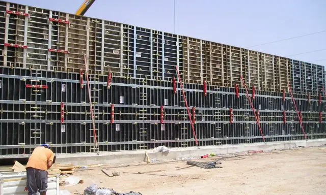 Trabajador supervisa el encofrar muro de gran tamaño, con estructura metálica y paneles negros, listo para el hormigón.