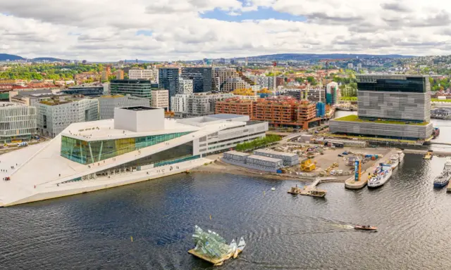 Il porto di Oslo con l'Opera House e moderni edifici. Barche navigano nell'acqua scura.