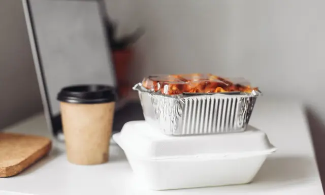 Gotowe jedzenie na wyjazd: zapiekanka w folii aluminiowej i kawa w kubku. Idealne na szybki lunch przy laptopie.