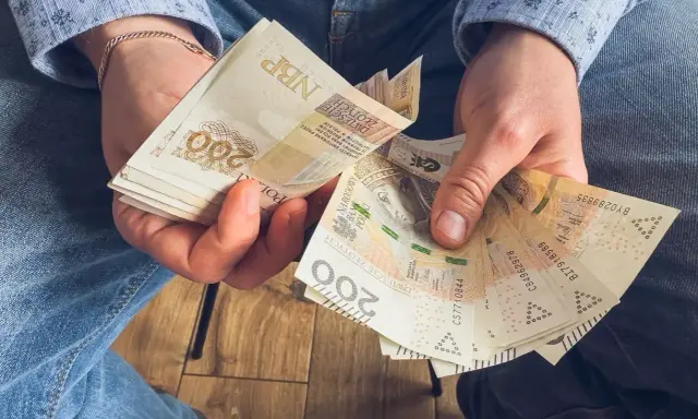 Ręce trzymające stos banknotów 200 zł. To może być wynagrodzenie za urlop, które pozwoli na zasłużony odpoczynek.