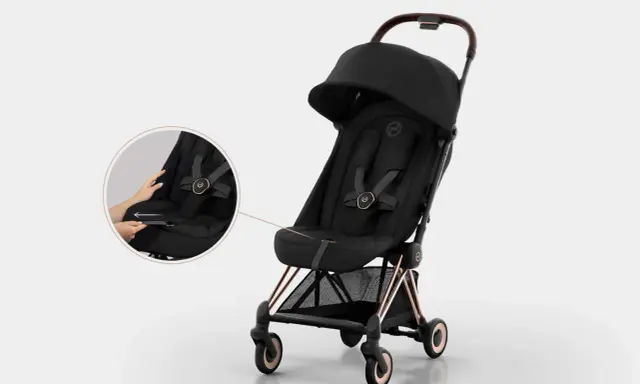 Elegancki czarny wózek Cybex Coya z miedzianymi detalami. Widoczna lupa pokazuje łatwe zapinanie pasów.