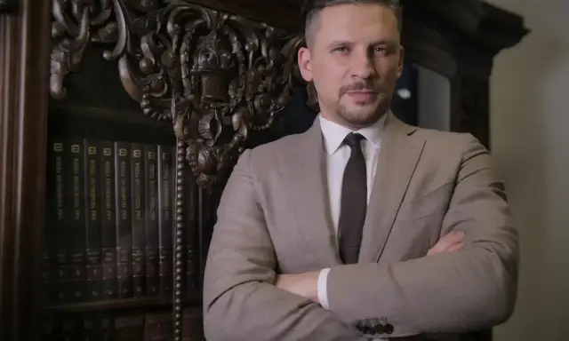 Mężczyzna w garniturze stoi przed regałem z książkami prawniczymi.
