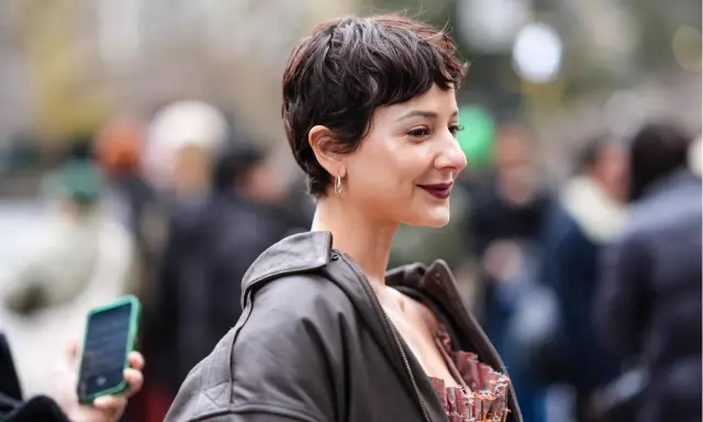 Frau mit einem lässigen Pixie-Cut, dunklem Lippenstift und Lederjacke lächelt in die Kamera.